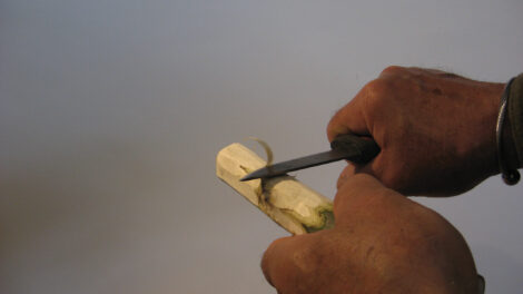 person cutting of a sliver of wood from a stick